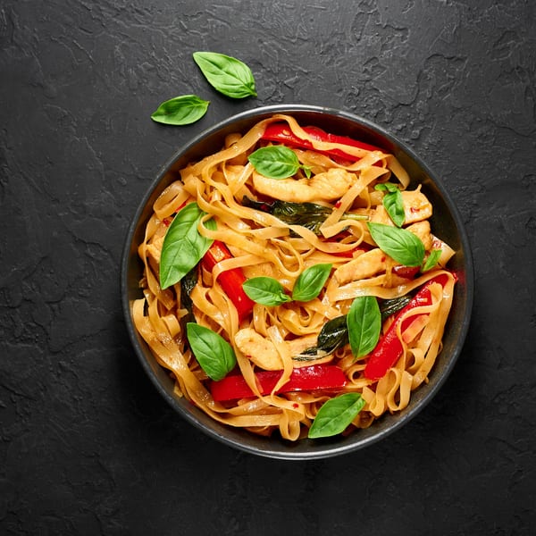 Thai Drunken Noodles with chicken, red bell peppers, and basil in a dark bowl.