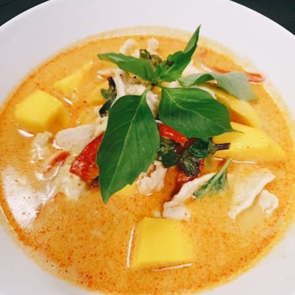 Thai mango red curry with chicken, red bell peppers, and basil in a white bowl.