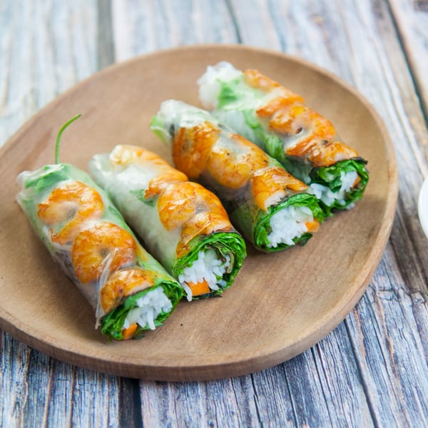 Four fresh Thai spring rolls with shrimp, rice, and vegetables on a wooden plate.