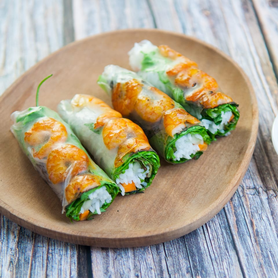 Four fresh Thai spring rolls with shrimp, rice, and vegetables on a wooden plate.