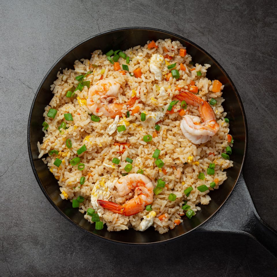 Thai shrimp fried rice with carrots, scrambled egg, and green onions in a black pan.