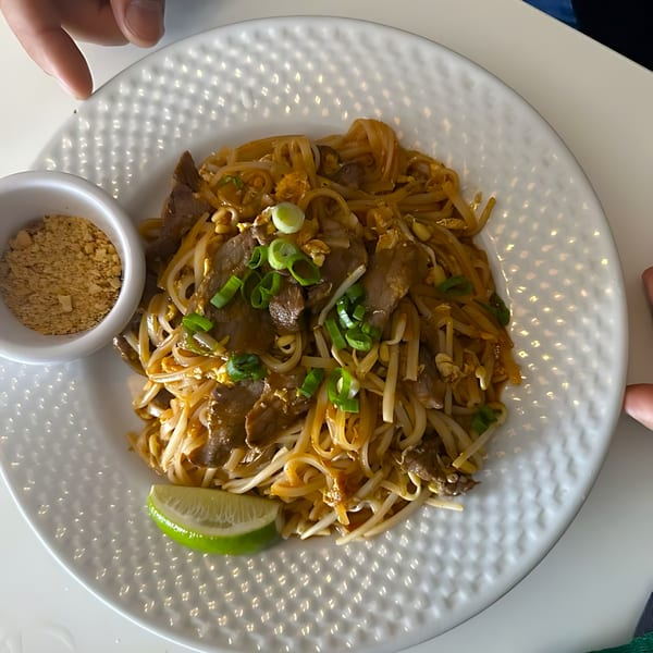 Pad See Ew with beef, bean sprouts, green onions, and a lime wedge, served with ground peanuts.