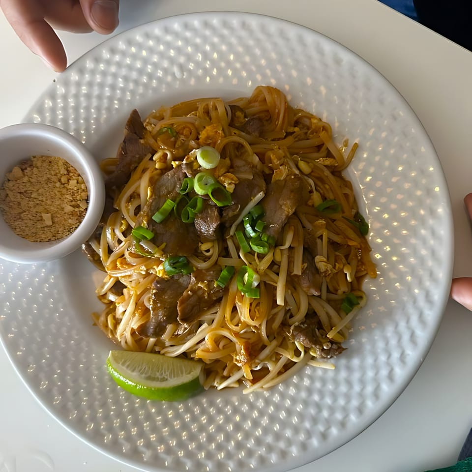 Pad See Ew with beef, bean sprouts, green onions, and a lime wedge, served with ground peanuts.